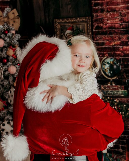Santa Claus is holding a young blonde girl who is looking at the camera.