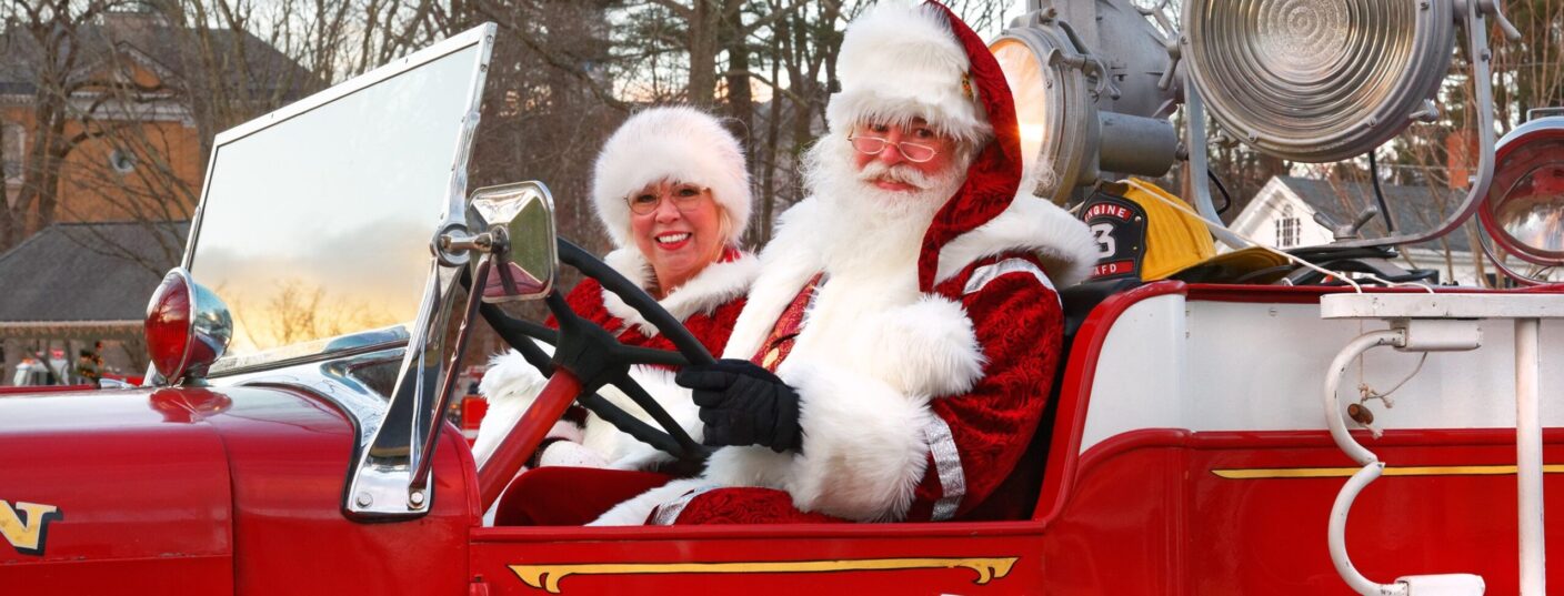 Santa and Mrs. Claus in a 1938 open cab fire truck. Santa is driving.