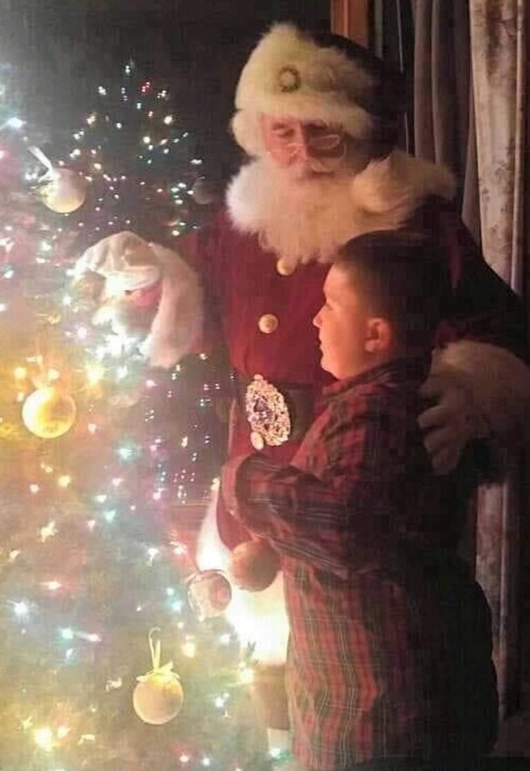 Santa and an older boy decorating a Christmas tree.