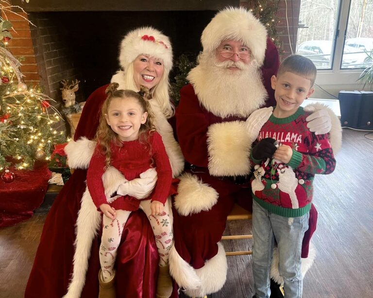 Santa and Mrs. Claus are posed with a young boy and girl and smiling for the camera.