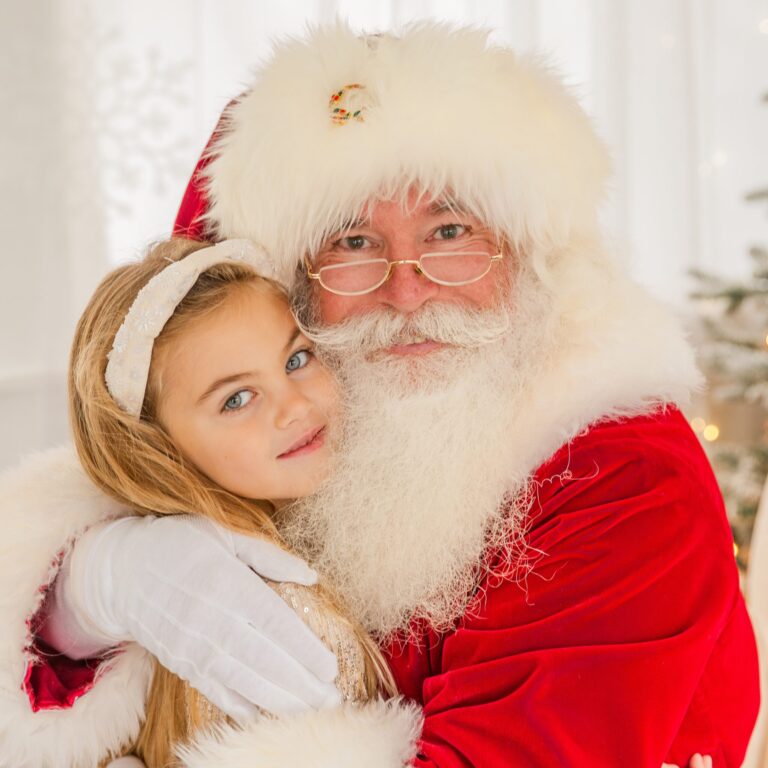 Santa Claus and a young girl are hugging and smiling for the camera.